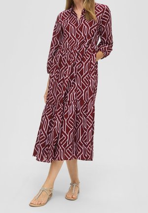 Vestido largo borgoña con un patrón geométrico blanco, botones en la parte delantera, cintura elástica, mangas largas y bolsillos laterales. Combinado con sandalias claras.