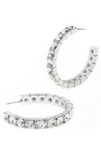 Runda silverfärgade hoopsörhängen med klara rhinestones i en flexibel design, med en slät metallicfinish och små hål längs kanten.