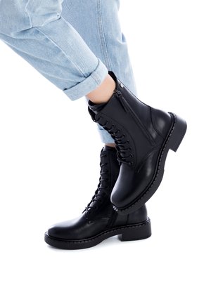 Musta nahkainen nilkkurit nauhoilla ja sivuvetoketjuilla, joissa on paksu pohja ja teksturoitu ompelu reunoilla.