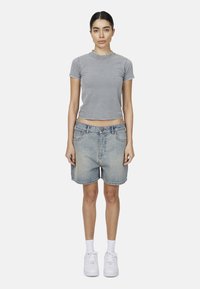 Szara, krótko rękawowa dopasowana koszulka z okrągłym dekoltem, połączona z jasnoniebieskimi dżinsowymi szortami. Białe sneakersy i białe skarpetki sięgające kostek dopełniają strój.