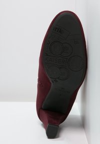 Bordeauxfarvet suedestøvle med hæl og en tekstureret gummisål, med diskrete syningsdetaljer og et strømlinet design.