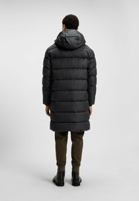 Abrigo largo negro acolchado con capucha, con acolchado horizontal y corte recto. Completa el look con pantalones oscuros y botas negras hasta el tobillo.