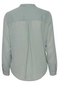 Blusa verde chiaro con colletto, maniche lunghe e orlo arrotondato. Presenta una piega sul retro e polsini con bottoni. Tessuto dalla texture liscia.