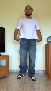 T-shirt branca de algodão, jeans de denim azul com um corte descontraído e ténis pretos com detalhes brancos. Fundo simples e móveis de madeira.