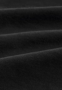 Close-up van zwarte stoffen vouwen die een zachte, lichtelijk gestructureerde oppervlakte tonen met een fijn weefpatroon en subtiele lichtreflecties.