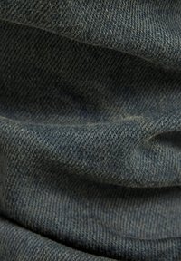 Tela de denim azul oscuro con una textura tejida que presenta costuras visibles, pliegues y un sutil sombreado, enfatizando su calidad material.