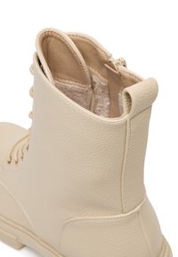 Botine din piele bej, cu finisaj texturat, dotate cu un fermoar parțial și șireturi, și un toc în buclă pentru o îmbrăcare ușoară.