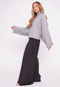 Szary sweter z dzianiny z wysokim kołnierzem i szerokimi rękawami, w zestawie z czarnymi spodniami o szerokich nogawkach. Gładka faktura i luźny krój.