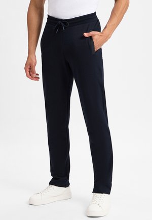 Navy Jogger aus weichem Stoff mit elastischem Bund und Kordelzug. Mit seitlichen Taschen und schmalem Bein design, kombiniert mit weißen Sneakern.