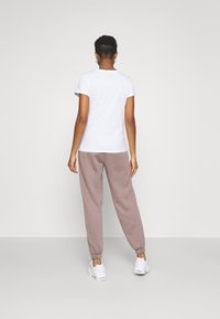 Vit t-shirt med korta ärmar kombinerad med ljusrosa mjukisbyxor. Byxorna har elastiska muddar och fickor. Skorna är vita sneakers.