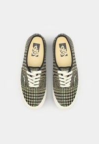 Canvas sneakers met een houndstooth-patroon in groen, zwart en crème, met witte veters en een rubberen zool.