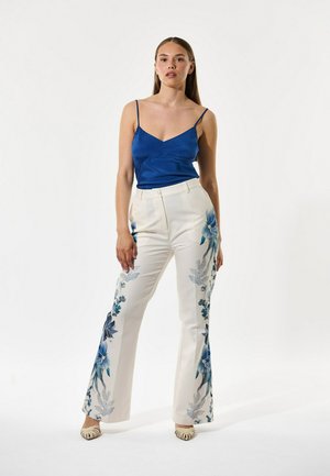 Modro satenasta majica na tanke naramnice, kombinirana z belimi razširjenimi hlačami z modrimi cvetličnimi potiski na straneh.