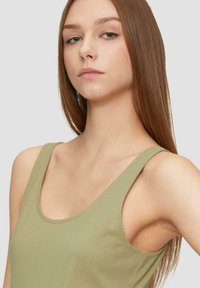 Débardeur vert olive sans manches avec un col rond et de larges bretelles. Fabriqué dans un tissu doux et lisse avec une silhouette ajustée.