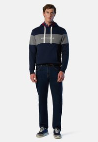 Hoodie bleu marine et gris avec des cordons blancs et le logo "NORTH SAILS", associé à un jean foncé et des baskets grises. Design décontracté avec poches.