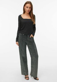 Czarny longsleeve z kwadratowym dekoltem, połączony z szerokimi spodniami pokrytymi srebrnymi cekinami. Modelka nosi czarne sandały na obcasie.