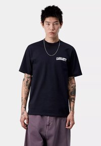 Granatowa bawełniana koszulka z krótkim rękawem, z białym logo "Carhartt" na lewej piersi. Prosty krój, minimalistyczny design.