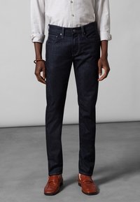 Mörkblå jeans av denim med rak passform, femfickorsdesign, subtila sömmar och bruna läderloafers som kompletterar outfiten.