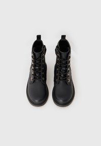 Schwarze Lederstiefeletten mit goldenen Ösen, runder Fußspitze und Schnürdesign. Mit einem Zugband an der Rückseite und einer strukturierten Sohle.