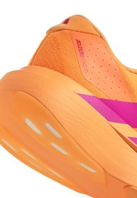 Running shoe featuring an orange upper made of textured material, with pink accents and a white rubber sole displaying cutouts.