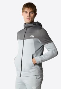 Felpa con zip grigia e grigio chiaro con design texture, cappuccio e tasche frontali. Presenta il logo The North Face sul petto.