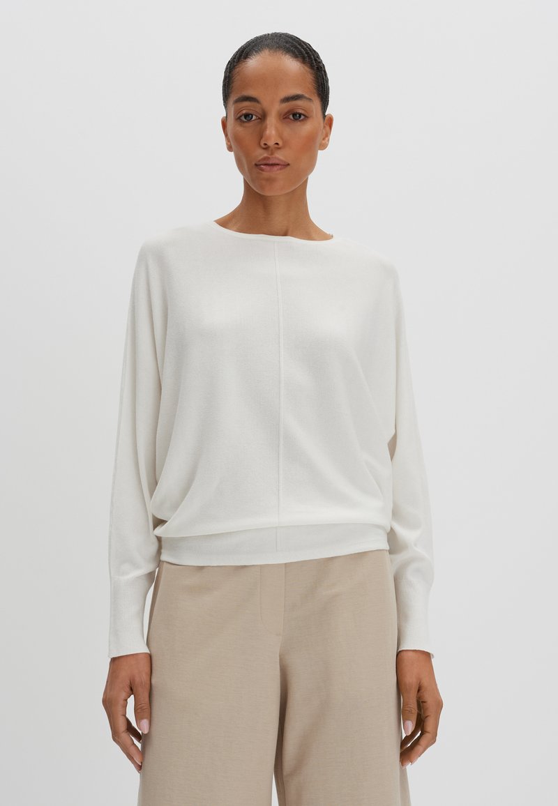 Biała, lekka dzianinowa bluzka z okrągłym dekoltem i długimi rękawami. Posiada luźny krój oraz subtelną detal w postaci szwu na środku.