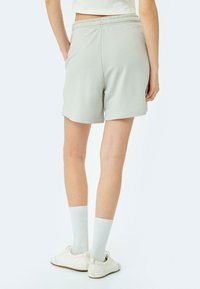 Pantalones cortos de algodón gris claro con cintura elástica, bolsillos laterales y un corte relajado. Llevados con calcetines blancos y zapatos.