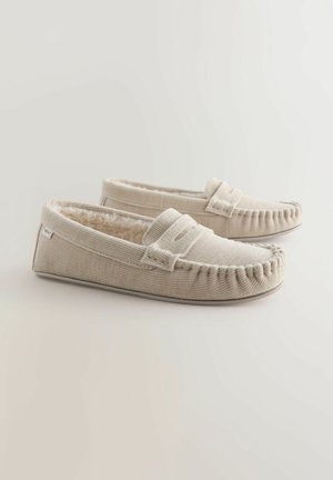 Chaussons en tissu beige avec une surface texturée, dotés d'une doublure en fausse fourrure confortable et de coutures décoratives le long des bords.