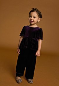 Violetter Samtoberteil mit Puffärmeln, Peplum-Taillierung und passenden schwarzen Samthosen; Leopardenmuster-Ballerinas mit dekorativem Akzent.