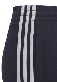 Joggers azul marino con una cintura acanalada y tres rayas verticales blancas a los lados. La tela parece suave con un acabado texturizado.