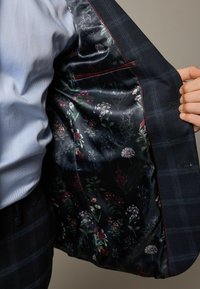 Mørkeblå ternet blazer med et blomstermønstret silkefor, der har rige farver, intrikate mønstre og en glat tekstur.