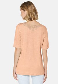 Kurzärmliges, pfirsichfarbenes T-Shirt mit einer Spitzenakzent am Ausschnitt. Leichtes Material, entspannte Passform, schlichte Rückseite.