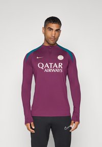 Maroonsininen pitkähihainen urheilupaita, jossa on puolivetoketju, tealmustat yksityiskohdat hartioissa ja "Qatar Airways" -logo rinnassa. Muotoilu on istuva.