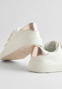 Baskets blanches en matériau synthétique lisse, dotées d'une semelle blanche texturée. Accents métaliques roses sur le talon et doublure intérieure douce.