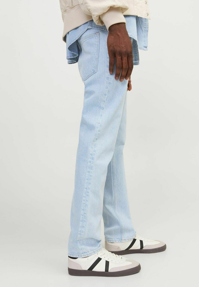 Jeans de pierna recta de color azul claro con una textura de denim suave, con costuras en contraste y bolsillos traseros, combinados con zapatillas blancas.