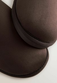 Dunkelbrauner Hausschuh mit glatter, weicher Textur; runde Form; mit einem dünnen Rand eingefasst. Verfügt über ein gepolstertes Design für Komfort.