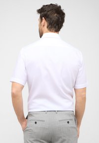 Witte overhemd met korte mouwen, een klassieke kraag en opgerolde mouwen, gecombineerd met lichtgrijze trousers met een gladde textuur en achterzakken.