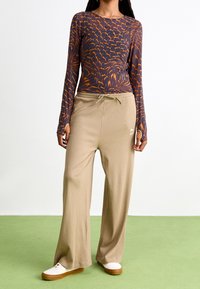 Långärmad topp med en mörkblå botten och ett mönster av orangea vågor, parat med ljusbeiga ribbade vida byxor med justerbar dragsko.