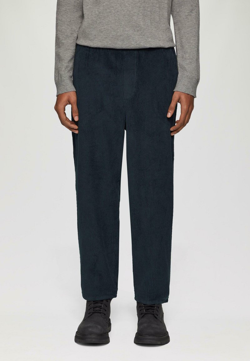 Pantalons en velours côtelé bleu marine avec des rayures verticales, design à jambes droites, taille élastique, associés à des bottes noires à lacets et à un pull gris.