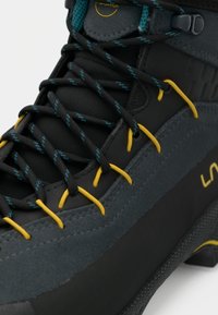 Melnas un pelēkas pārgājienu zābaki, kuriem ir teksturēta virsma, dzelteni un tumši zili šņorējumi, kā arī pastiprināta aparatūra. Virsma ir izgatavota no sintētiskā materiāla.