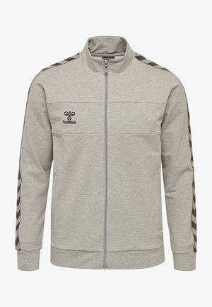 Chaqueta gris con cremallera, hecha de material de sudadera, que presenta un cuello alto, un patrón de chevrón negro en contraste a lo largo de las mangas y un logo en el pecho.