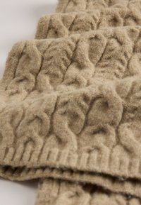 Beige knit scarf made of soft wool, featuring a textured cable pattern with raised designs, and a ribbed edge.