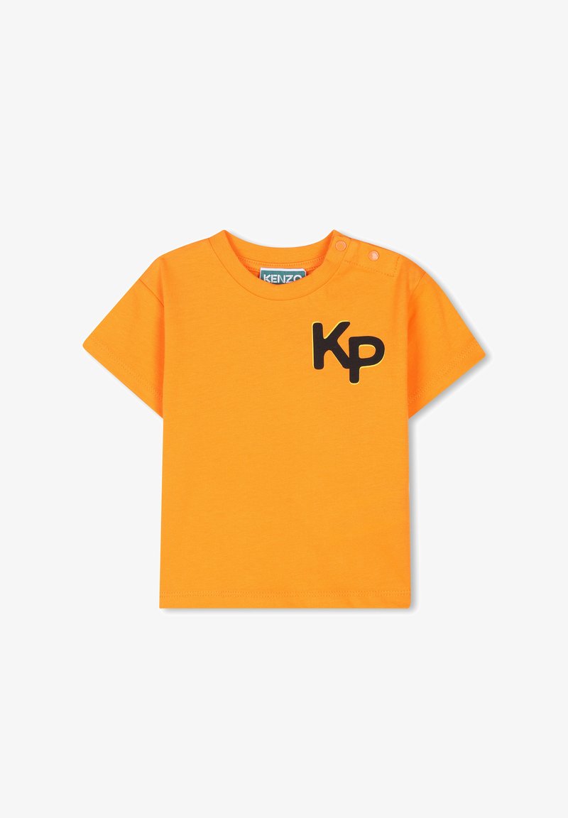 T-shirt en coton orange avec des manches courtes, un col rond et un logo noir "Kp" sur le devant. Comprend deux boutons-pression sur l'épaule.