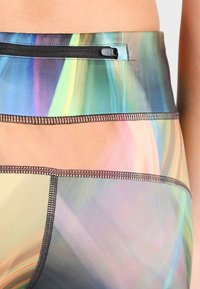 Zbliżenie wielokolorowych legginsów sportowych z czarną kieszonką na zamek błyskawiczny w pasie i widocznymi detalami przeszycia.