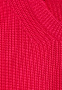 Maglione fucsia lavorato a maglia con texture a coste e design a V. La superficie presenta un motivo uniforme di punti in rilievo.