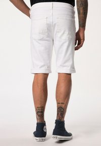 Pantalones cortos de mezclilla blanca con dobladillo enrollado, que presentan bolsillos traseros y un ajuste ceñido. Se lleva un par de zapatillas altas azules.