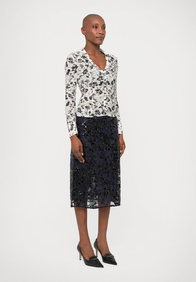 Floral-patterned button-up top in white and black, paired with a sheer black sequined midi skirt and black pointed-toe heels.
