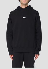 Felpa nera con tasca a marsupio frontale, dotata di un piccolo logo bianco sul petto, maniche a costine e taglio rilassato. Materiale morbido.