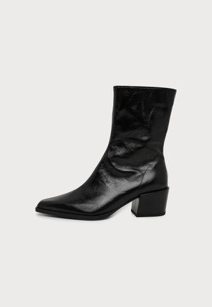 Botte en cuir noir brillant mi-mollet avec bout pointu et talon bloc, vue de côté sur un fond clair uni.