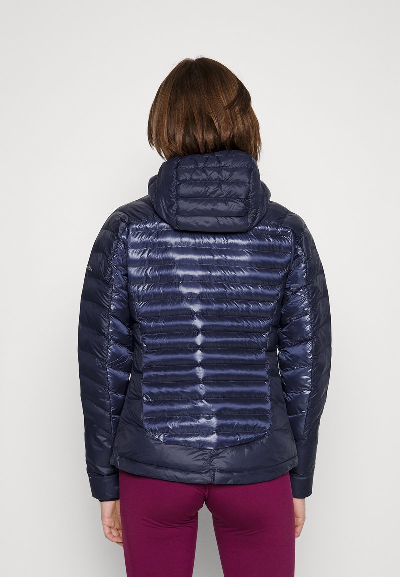 Veste doudoune navy avec une texture matelassée, une capuche et un matériau léger. Présente des coutures horizontales et une silhouette ajustée.