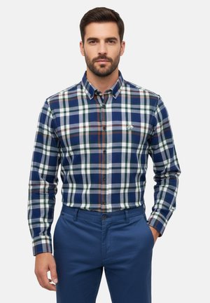 Camisa de hombre abotonada en tejido de cuadros azul, verde y blanco, con un logo bordado, combinada con pantalones azul marino.